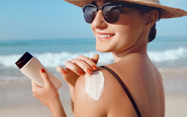 Frau am Strand cremt sich die Schulter mit Sonnencreme ein